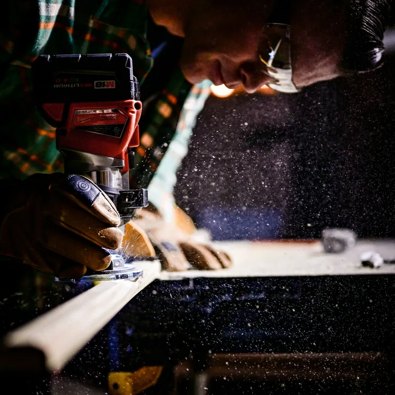 A tradesman running a compact router along the edge of a board