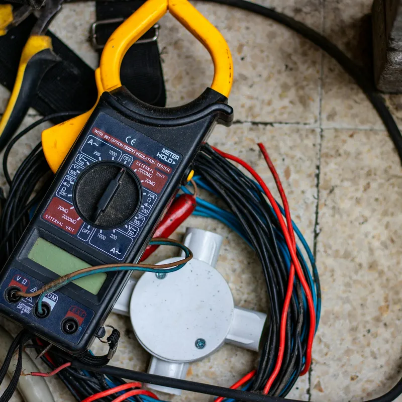 A clamp meter, pliers and coiled wire laid out beside a junction box