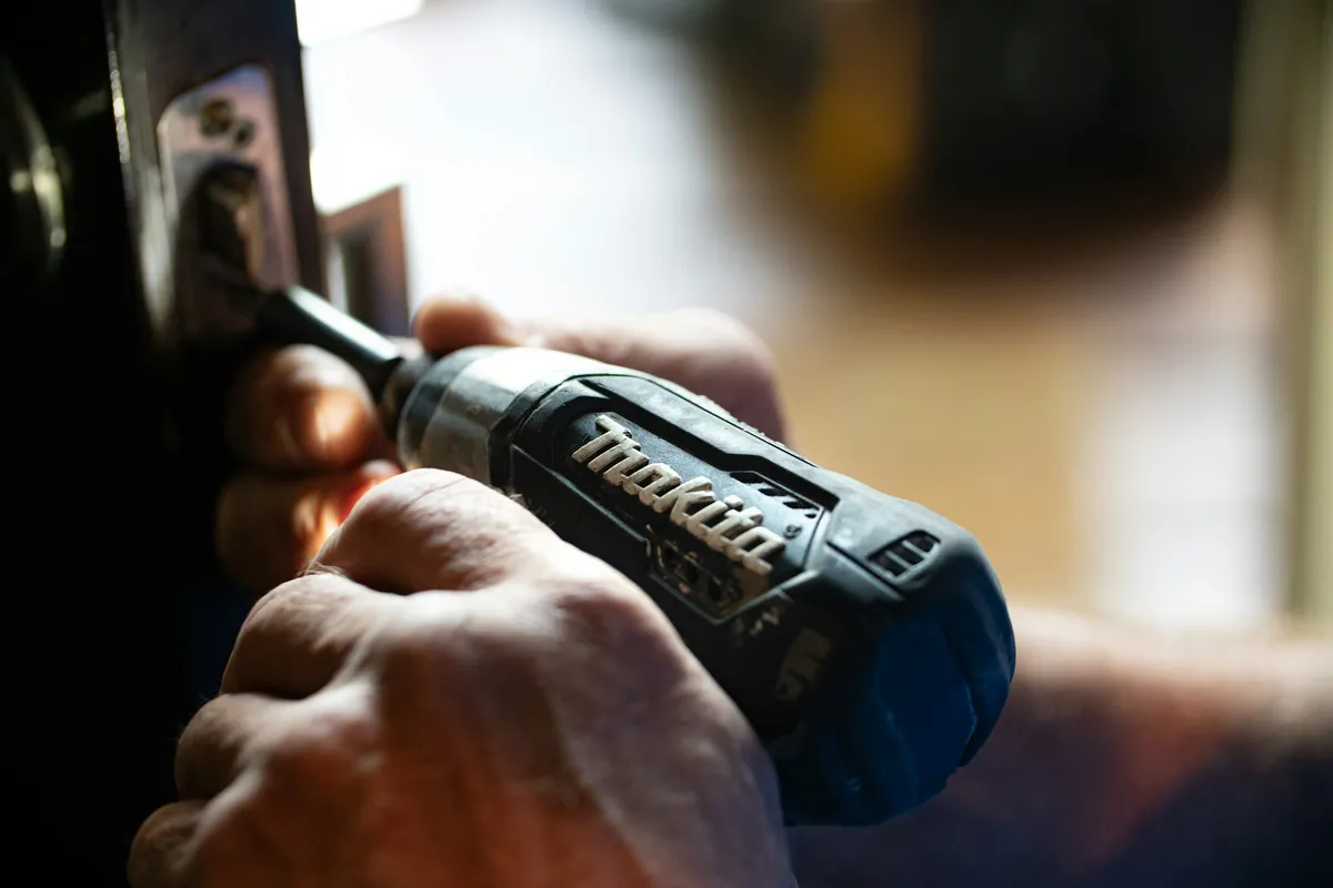 A close-up of a hand driving a screw with a cordless driver