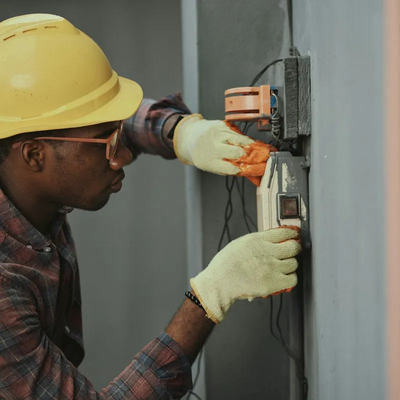 An electrician in a hard hat working on a wall-mounted switch box