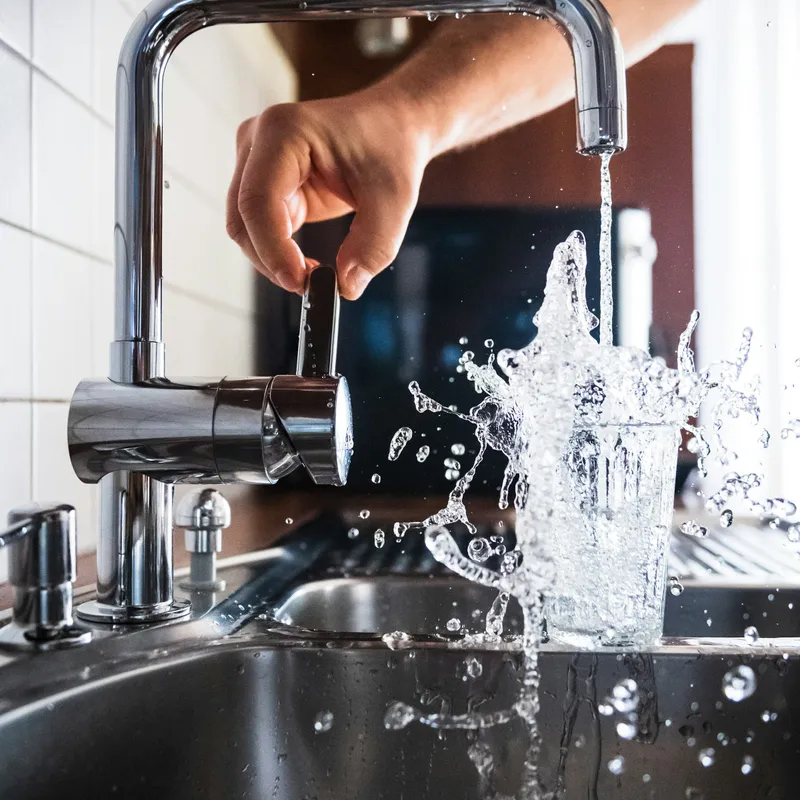 A kitchen faucet running into a glass at the sink